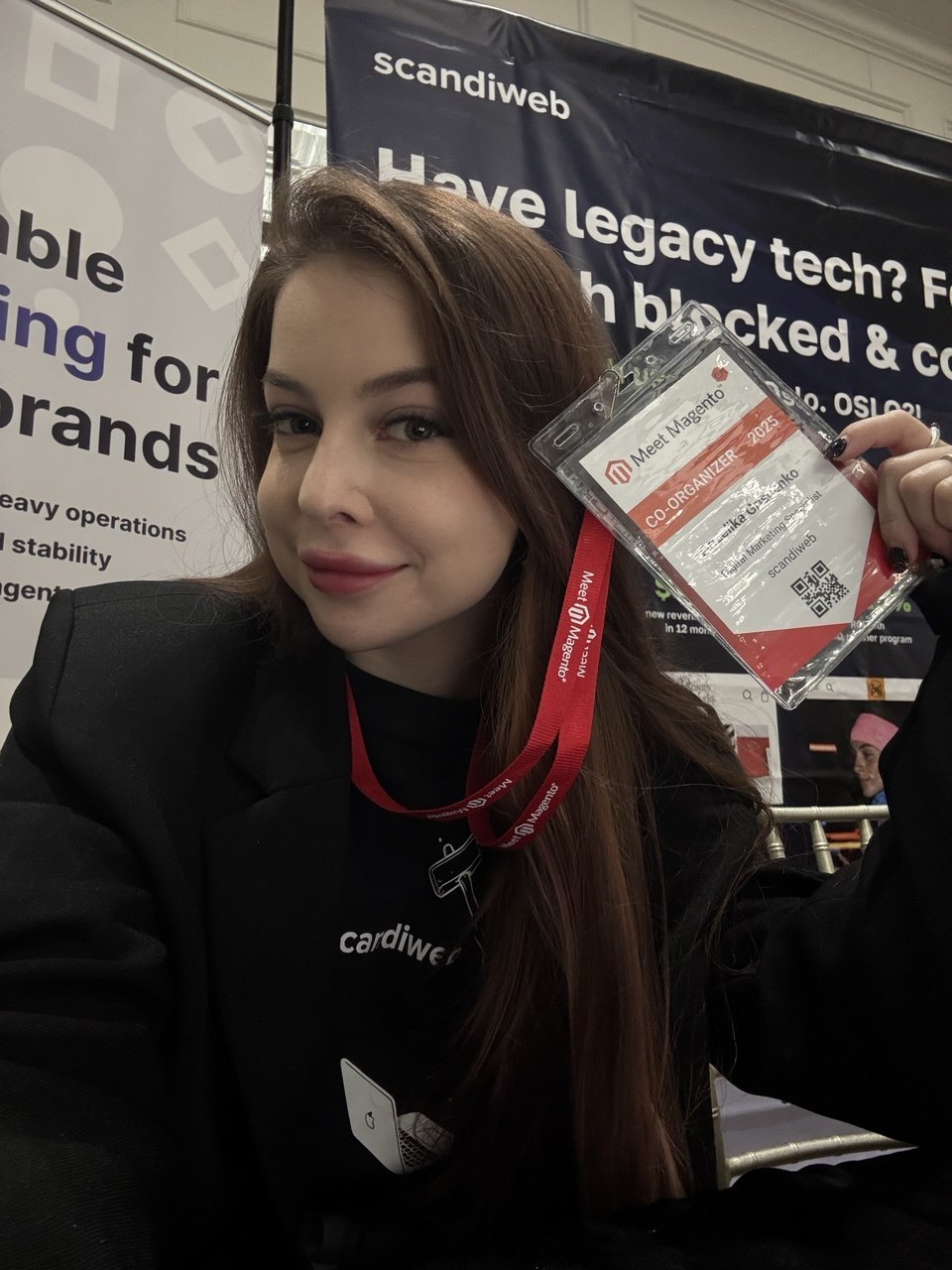 Anzelika holding her Meet Magento Canada 2025 co-organizer badge at the scandiweb booth